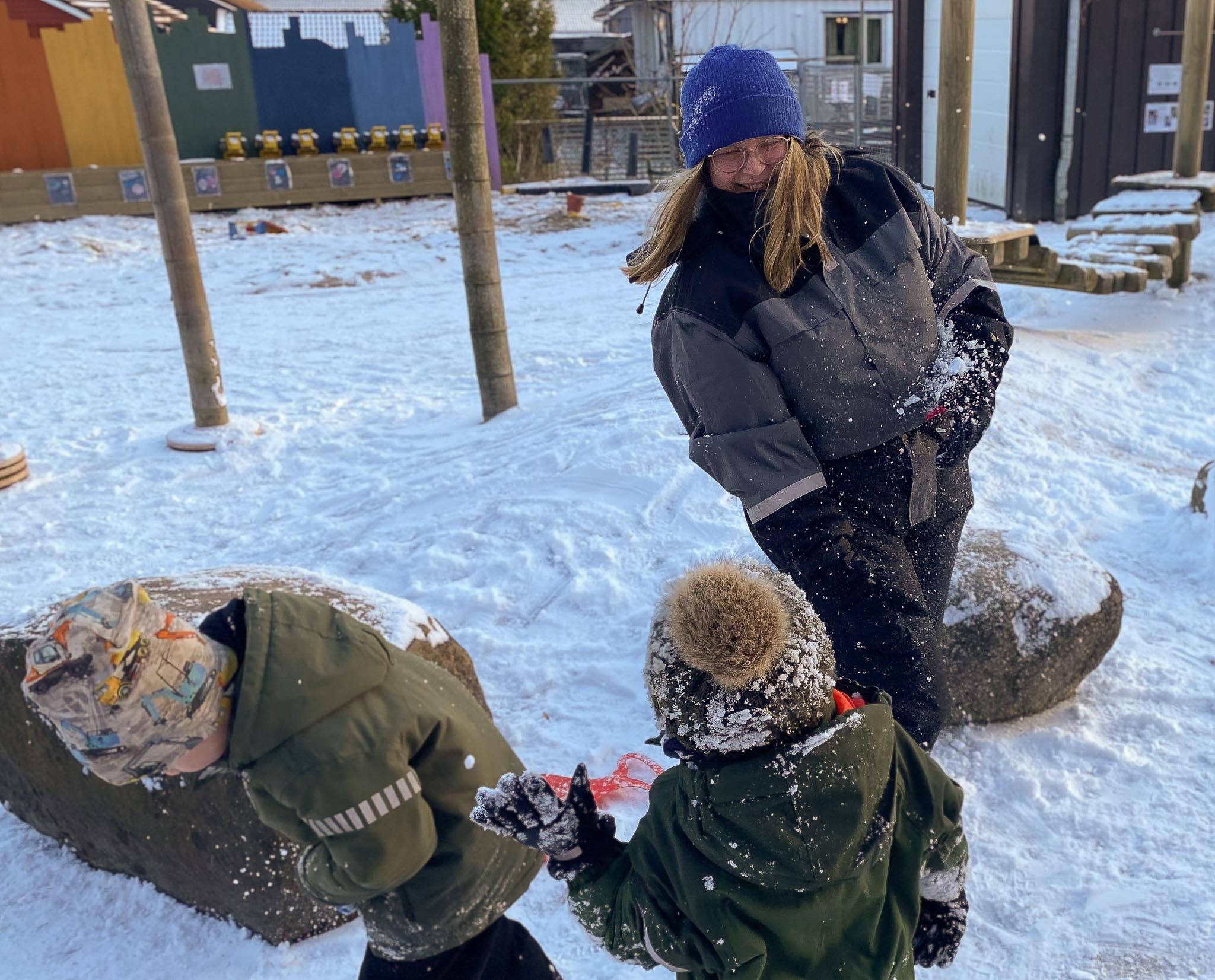 Ung kvinnelig barnehagelærerstudent er i praksis i barnehage. Uteområde, snø og snøkballkrig med barn