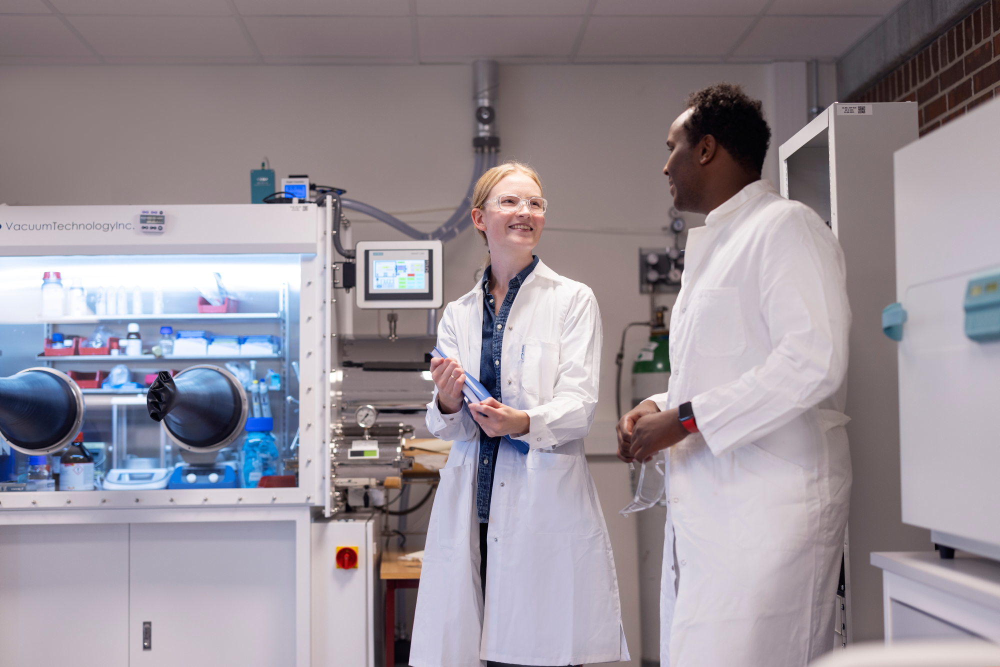 To studenter iført labfrakker i et laboratorium.