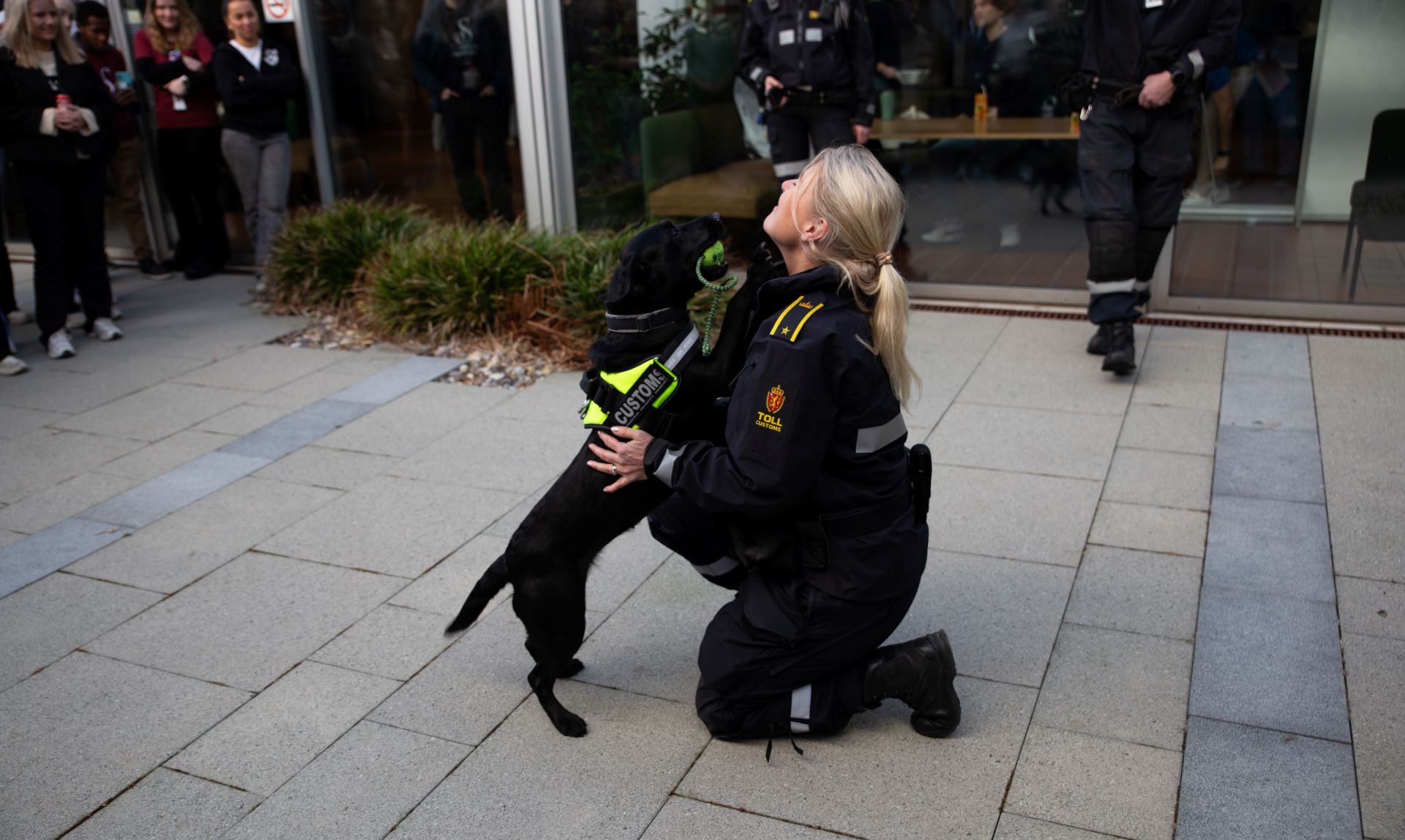 Hund og kvinne fra Tolletaten. Personer står i ring rundt. 