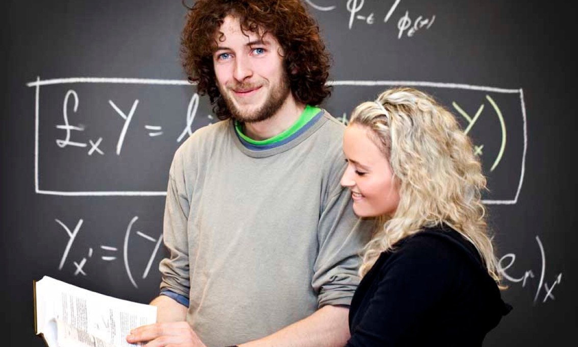 Kvinne og mann står sammen foran en tavle med matematikk på.