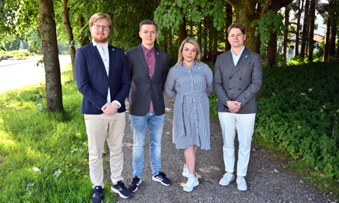 Fire studenter på rekke med gress og trær rundt