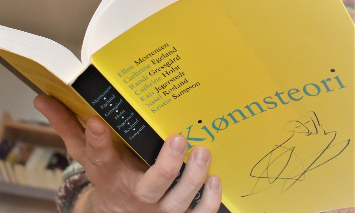 En person som holder en gul bok med tittelen "kjønnsteori"