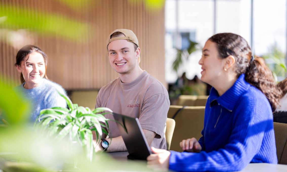 Tre studenter sitter sammen ved et arbeidsbord